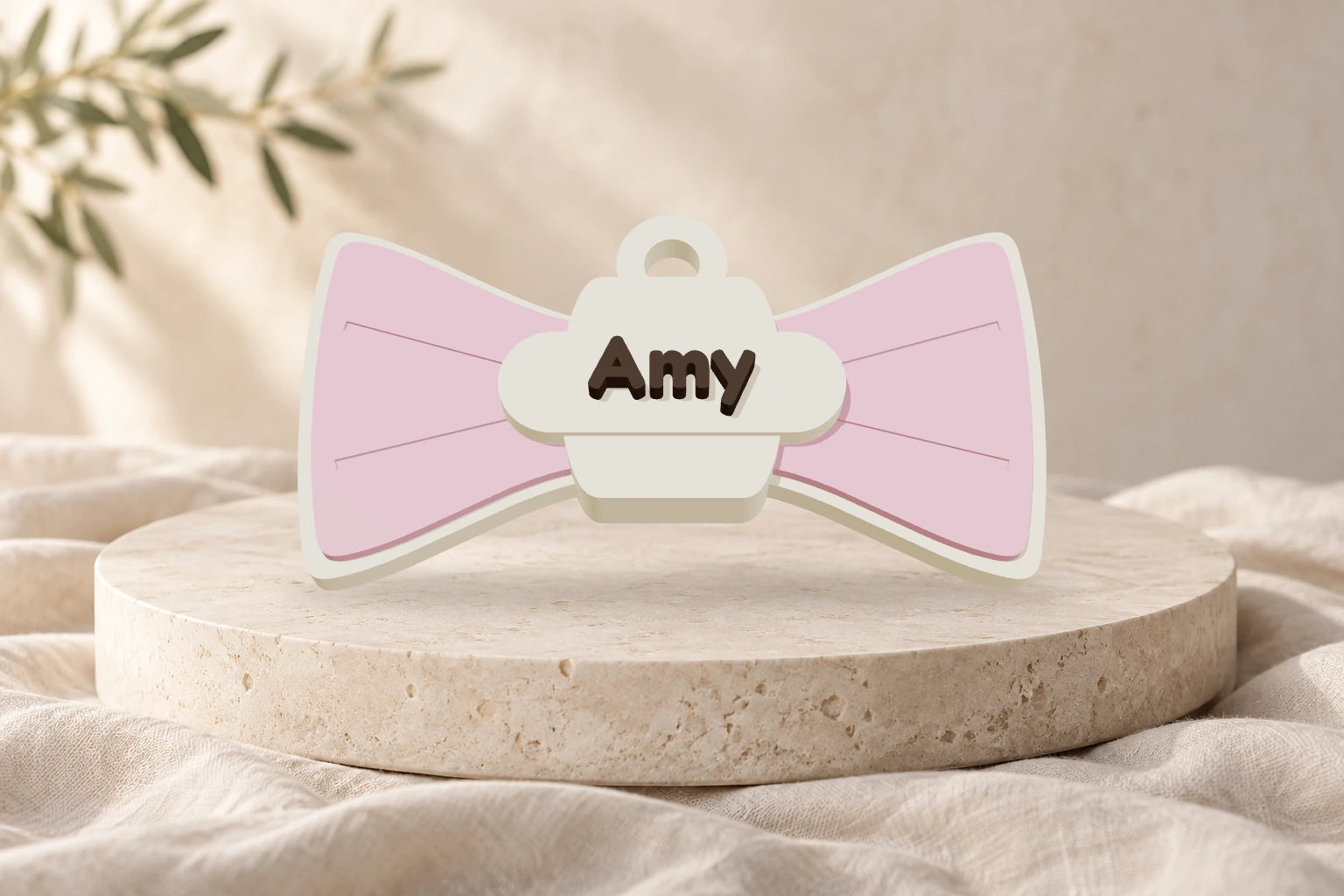 Zauberschleife als Anhänger in Sakura-Pink und Elfenbeinweiß mit dem Namen Amy auf einem hellen Steinpodest